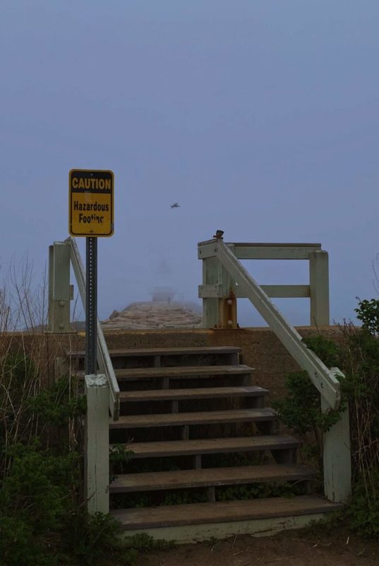 Stairs leading to the fog, with a sign that says, "Caution Hazardous Footing"